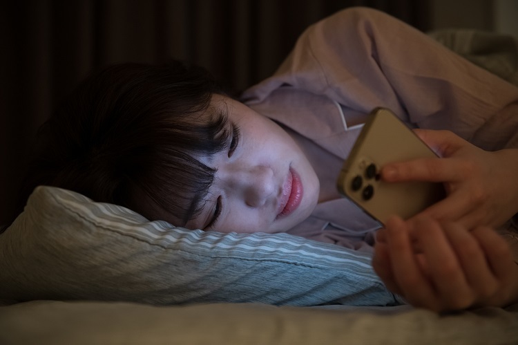 寝ながらスマートフォンを見る女性
